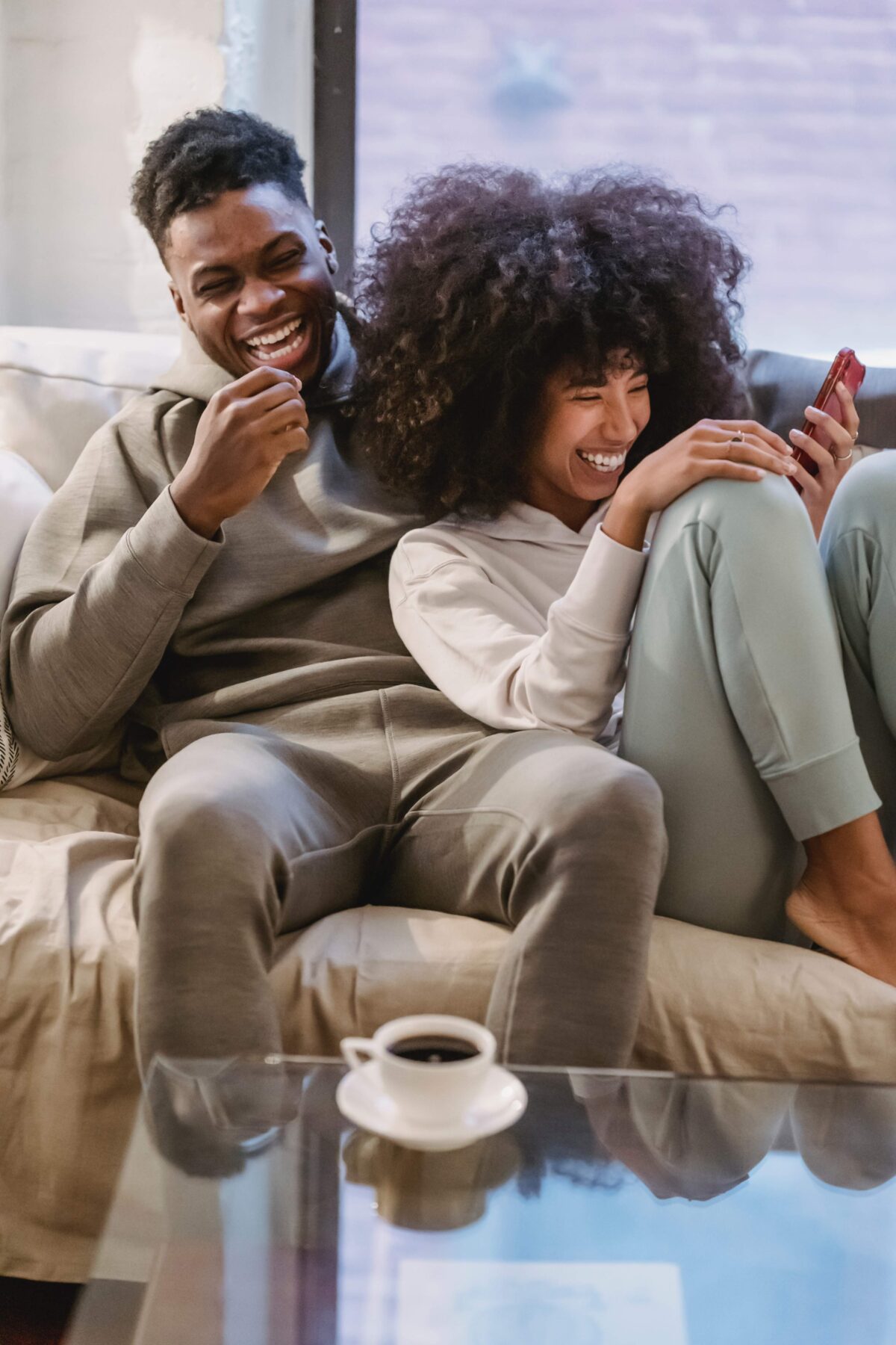 Couple sitting on a couch laughing and looking at a cell phone